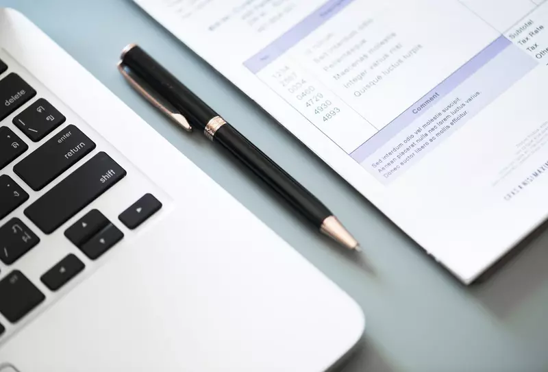 Fragment laptopa, dokumentu i długopis na biurku