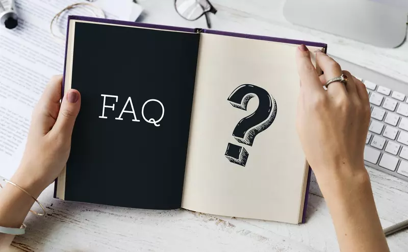 Kobiece dłonie trzymające otwarty notes z napisem FAQ i znakiem zapytania