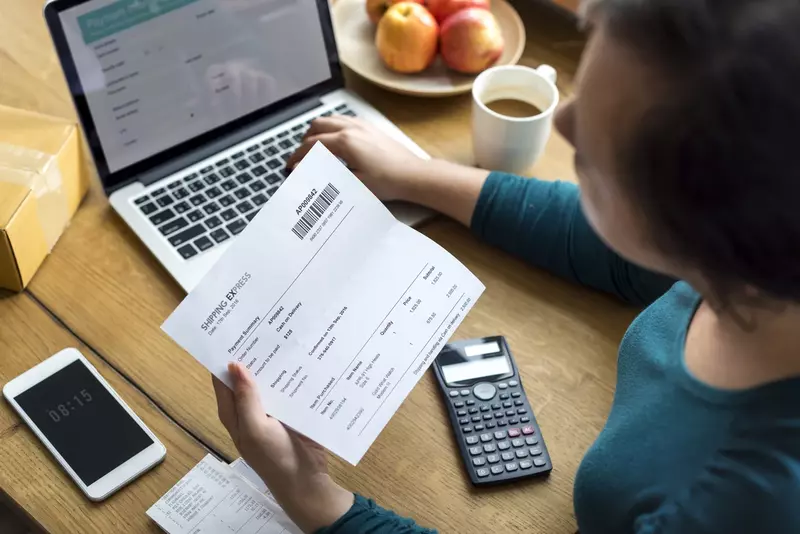 Kobieta w turkusowej bluzce trzymająca dokument, obok laptopa i kalkulatora