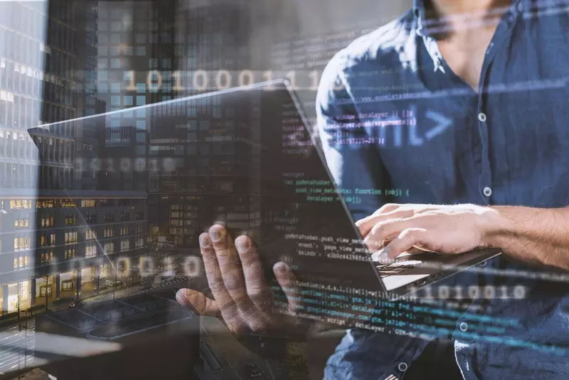 Człowiek trzymający komputer na drugim planie, na pierwszym kod html