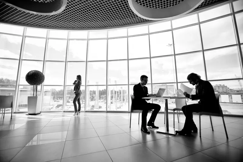 Dwóch mężczyzn siedzących przy stoliku przed laptopem w pomieszczeniu z wielkimi oknami