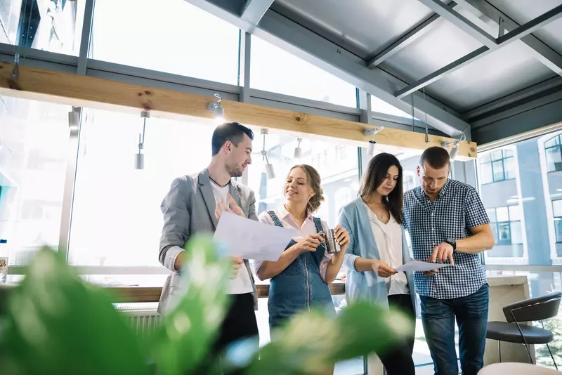 Czwórka osób w biurze stojąca i patrząca w dokumenty