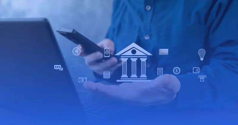 Mężczyzna ze smartfonem przy laptopie, nad otwartą dłonią ikona banku otoczona symbolami płatności i finansów