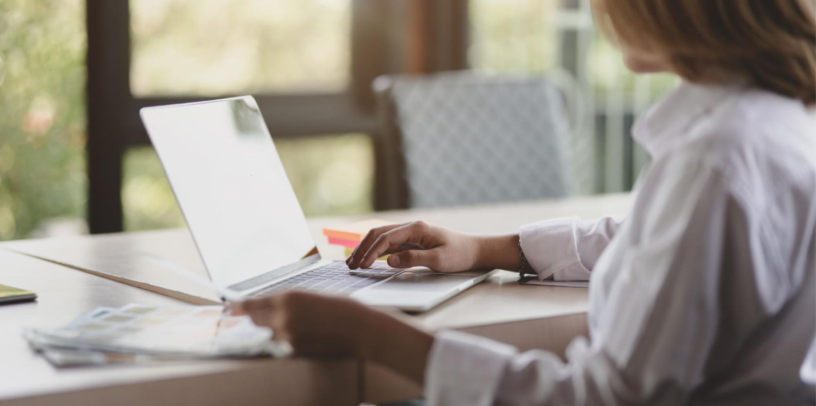 Kobiet siedząca bokiem przy laptopie w białej koszuli biznesowej