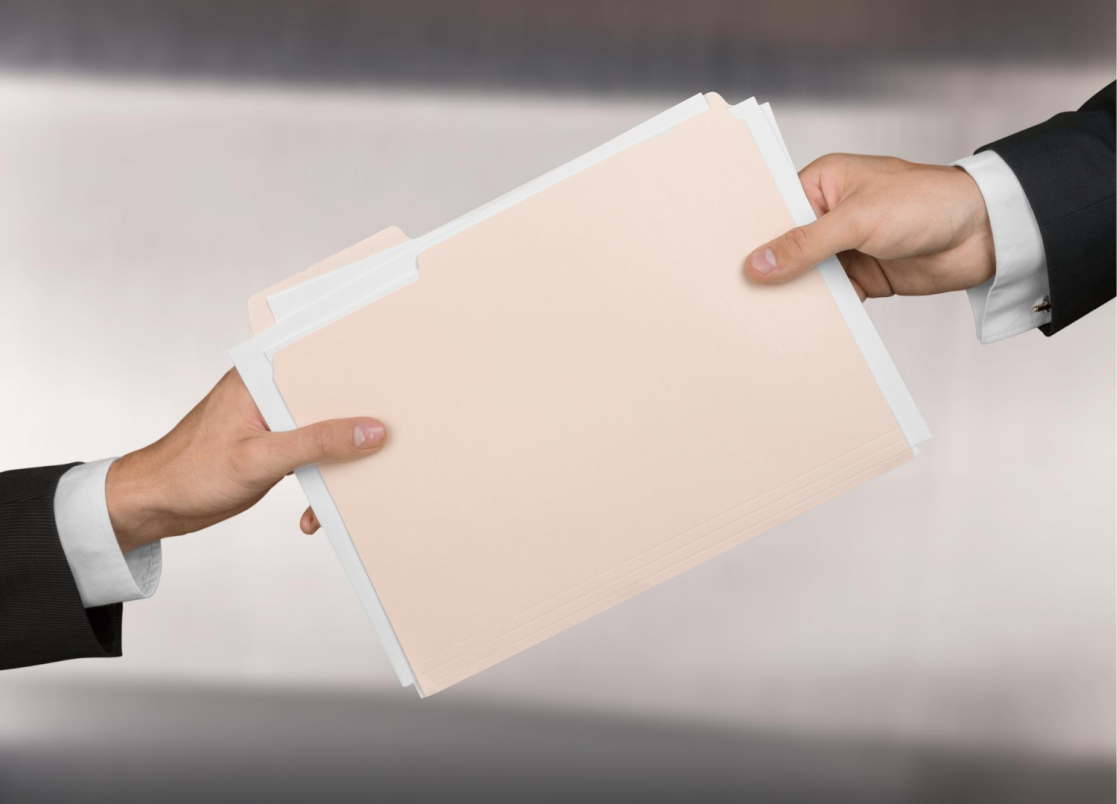Dwie męskie dłonie w garniturach przekazujące sobie żółtą teczkę z dokumentami