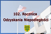 3 flagi przed urzędem gminy Wiśniew z herbem gminy i napisem 102. Rocznica Odzyskania Niepodległości