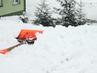 Zdjęcie fragmentu posesji, na której leży śnieg i łopata do odśnieżania.