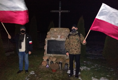 Zdjęcie dwóch mężczyzn przy pomniku w nocy z flagami Polski